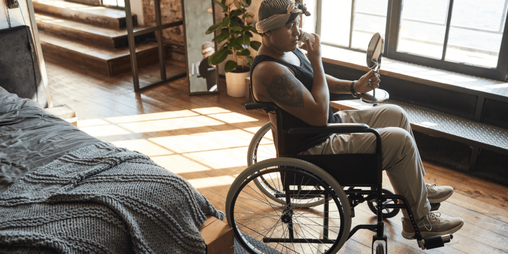 person of color in a wheelchair holding a mirror and applying their makeup