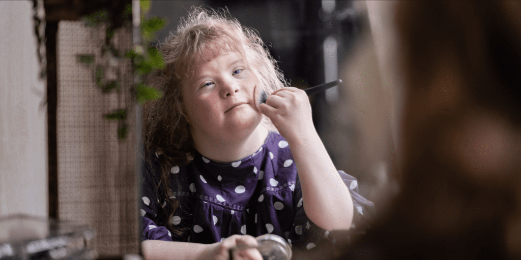 blonde woman with down syndrome applying makeup with a brush 